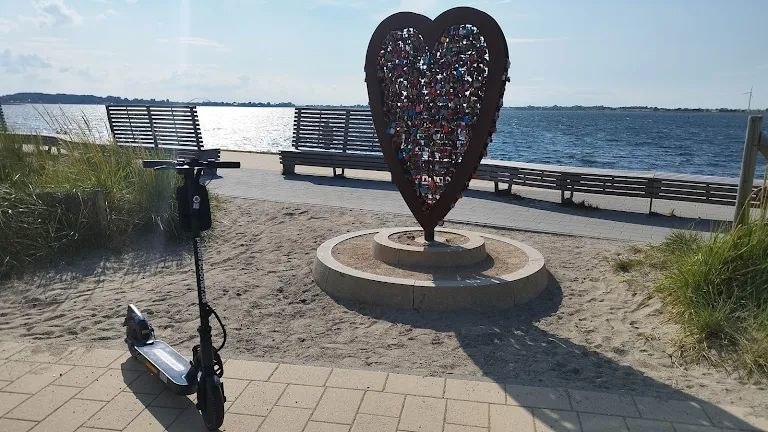 E-Scooter vor einer Herzskulptur an einer Uferpromenade